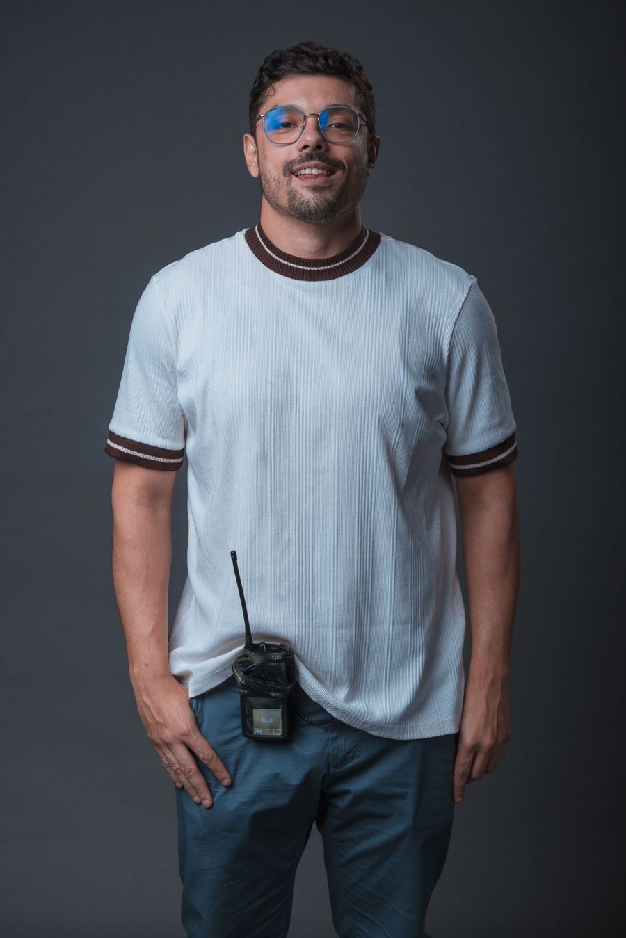 Victor Luporini de óculos e camiseta clara, sorrindo, em retrato de estúdio